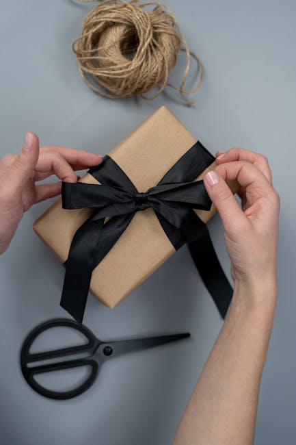 Home Hands tying a black ribbon on a craft paper gift box, next to scissors and twine.